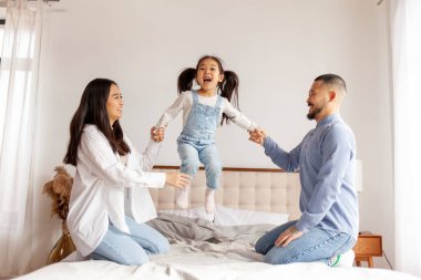 Mutlu Asyalı bir aile kızı ile oynuyor ve evde yatakta eğleniyor. Aktif Koreli küçük bir kız yatağa atlıyor ve çığlık atıyor.