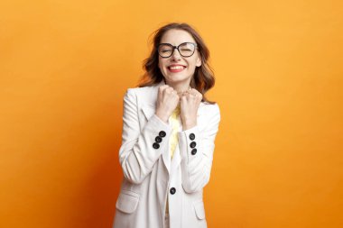 young business girl in glasses and white suit celebrating victory on colored isolated background, woman manager in blazer wins and shows gesture of success