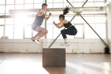 young beautiful athletic couple in sportswear at crossfit training in the fitness room, woman and man together at fitness training jump on the box in the morning