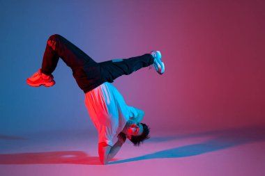 dancer doing acrobatic trick and dancing breakdance in neon red and blue lighting, young energetic guy stands on his hands in unusual pose, street style