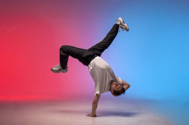 dancer doing acrobatic trick and dancing breakdance in neon red and blue lighting, young energetic guy stands on his hands in unusual pose, street style