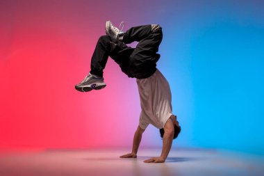 dancer doing acrobatic trick and dancing breakdance in neon red and blue lighting, young energetic guy stands on his hands in unusual pose, street style