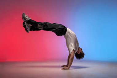 dancer doing acrobatic trick and dancing breakdance in neon red and blue lighting, young energetic guy stands on his hands in unusual pose, street style