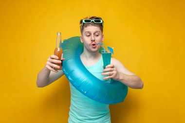 portrait of a young guy on vacation in the summer with a blue cocktail, a man with an inflatable ring holds a refreshing drink on a yellow background