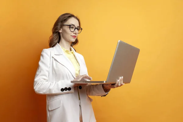 眼鏡と白いスーツの若いビジネスの女の子は 色の隔離された背景にラップトップを使用しています コンピュータでオフィススタイルの仕事の女性マネージャー — ストック写真