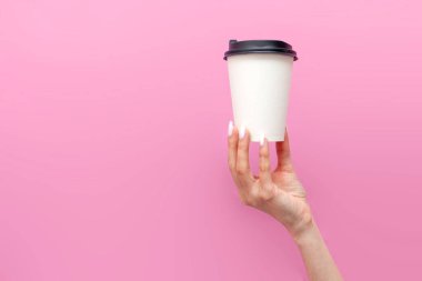 Pembe izole edilmiş arka plandaki kadının ellerinde beyaz, boş bir kahve fincanı. Kızın elleri tek kullanımlık karton bardağı içecek ve reklam alanı ile birlikte tutuyor.