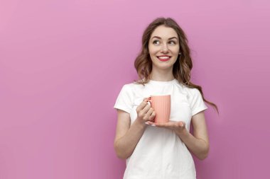 Genç düşünceli bir kadın elinde kahve bardağıyla fotokopi odasına bakıyor. İçkili beyaz tişörtlü kız pembe izole edilmiş arka planda düşünüyor ve hayaller kuruyor.