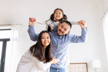 Mutlu Asyalı bir aile ve küçük bir kızı evde durup sevinirler, anne ve baba çocuğu kollarına alır ve gülümserler, aile evi konforu ve bakımı