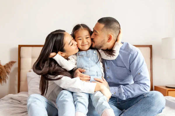 stock image happy young asian family sit on bed together with daughter, korean little girl hug and love parents at home, mom and dad kiss daughter