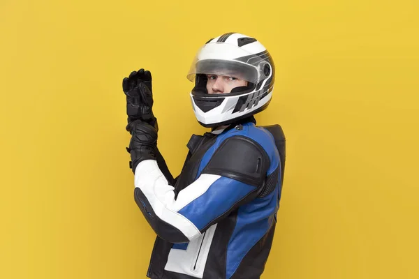 革のジャケットとヘルメットの若い男のオートバイのレーサーは黄色の隔離された背景に保護手袋を置き 保護具のプロのオートバイレーサー — ストック写真