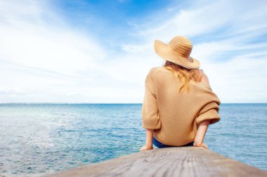 Denizdeki kız ufka bakıyor, güneş şapkalı kadın yazın iskelede oturuyor ve hayaller kuruyor, tatil konsepti, kopyalama alanı