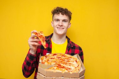 Öğrenci sarı arka planda pizza yiyor, kıvırcık bir genç fast food reklamları yapıyor ve gülümsüyor.