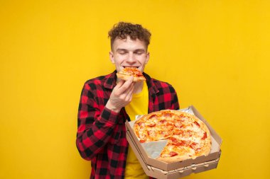 Sarı arka planda pizza yiyen genç, aç bir öğrenci fast food yiyor.