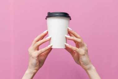 Pembe izole edilmiş arka plandaki kadının ellerinde beyaz, boş bir kahve fincanı. Kızın elleri tek kullanımlık karton bardağı içecek ve reklam alanı ile birlikte tutuyor.