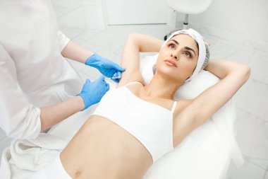 Doktor kozmetik uzmanı kozmetoloji kliniğindeki hastanın koltukaltına botulinyum toksini enjekte ediyor. Kozmetolojide hiperhidroz tedavisi görüyor.