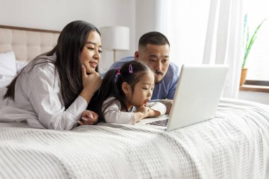 Mutlu genç Asyalı aile evde dizüstü bilgisayar kullanıyor, Koreli baba ve küçük kız bilgisayar ekranına bakıyor ve internetten çalışıyor.