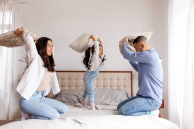 Yastık savaşı, küçük Asyalı kız evde ailesiyle oynuyor, Koreli ebeveynler kızlarıyla vakit geçirip seviniyor, anne ve baba çocukla eğleniyor.