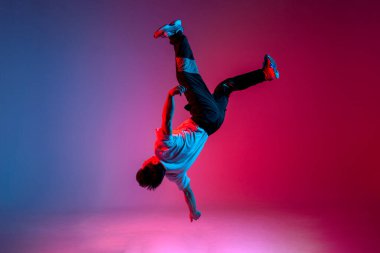 Adam akrobatın sırt yağını yeni ışıklandırmada yapıyor, erkek dansçı kırmızı arka planda zıplıyor ve havaya düşüyor, hiphop sanatçısı hile yapıyor ve havada uçuyor.