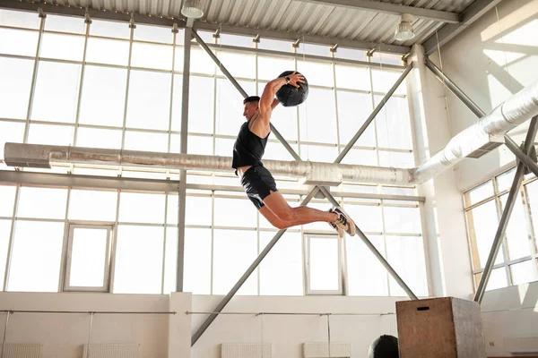 stock image athletic guy at crossfit training jumps and throws medicine ball in the gym, strong man is doing fitness with ball and doing sports exercise in a jump