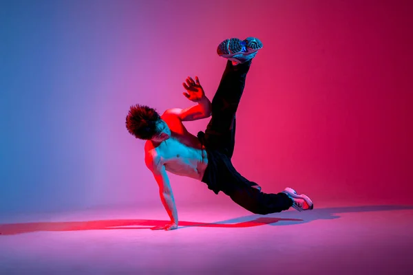 stock image young guy hiphop performer break dance in neon club lighting and doing acrobatic trick, male dancer stands in acrobatic pose