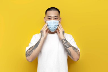 Tıbbi maskeli Asyalı adam ve beyaz futbol sarı izole edilmiş arka planda duruyor. Virüs ve gribe karşı koruyucu maskeli Koreli adam.