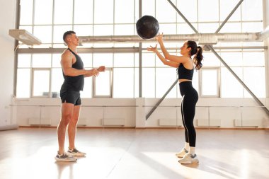 young beautiful athletic couple in sportswear at crossfit training throw the ball in the fitness room, woman and man together at fitness training with ball in the morning
