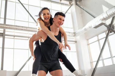 Spor giyim sektöründe genç ve mutlu bir çift koşuyor ve spor salonunda seviniyor. Adam kızı sırtında taşıyor ve gülümsüyor. Özgürlük kavramı.