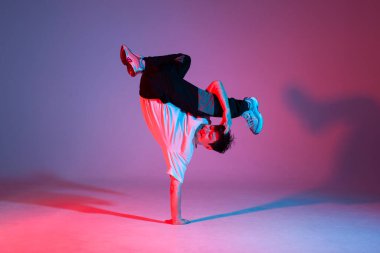 Genç erkek dansçı neon ışıkta dans ediyor, erkek akrobat kırmızı arka planda dans ediyor, hip hop sanatçısı hareket ediyor ve elleri üzerinde duruyor.