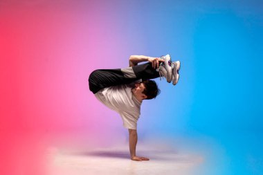dancer doing acrobatic trick and dancing breakdance in neon red and blue lighting, young energetic guy stands on his hands in unusual pose, street style