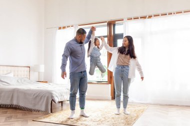 Ebeveyn sevgisi ve bakımı, mutlu Asyalı aile küçük kızıyla oynar ve onu kollarına alır. Küçük kız, anne ve babasıyla evde, yatak odasında eğlenir.