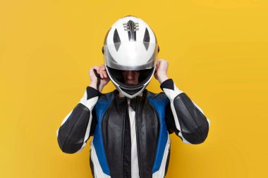 Deri ceketli genç motosikletçi sarı izole edilmiş arka planda miğfer takıyor, koruyucu kıyafetli profesyonel yarışçı miğfer tutuyor, kopyalama alanı kullanıyor.