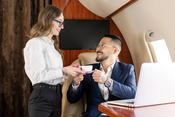 air hostess woman gives coffee to businessman on plane, asian manager in suit flies in private jet and orders coffee, luxury lifestyle
