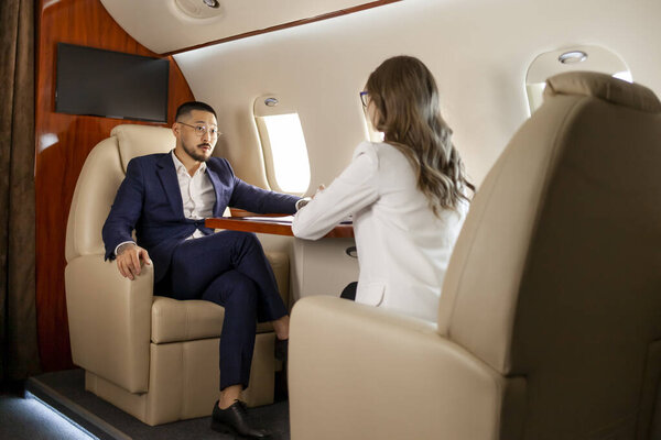 деловая встреча в самолете, азиатский бизнесмен в костюме беседует с деловым партнером и обсуждает сделку, деловые люди летают на частном самолете и общаться