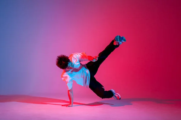 stock image young guy dancer is dancing break in neon lighting, male acrobat is doing trick and dance exercise on red blue background, hip hop performer is moving and standing on his hands