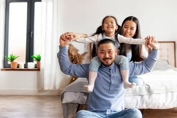 stock image Korean dad holds his little daughter in his arms and depicts flight, the child plays with his parents and rejoices at home near the bed, happy Asian family