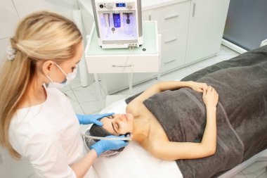 Doktor kozmetik uzmanı, kızın yüzünü kozmetoloji kliniğindeki hastaya vakum temizliği yaparak temizliyor.