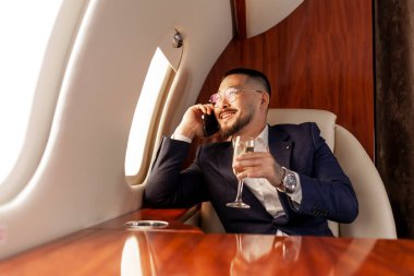 Asyalı işadamı özel lüks bir jetle uçuyor ve telefonla konuşuyor ve şampanya içiyor, takım elbiseli Koreli girişimci ve gözlükler takıyor ve cep telefonu iletişimiyle uçakla iletişim kuruyor.