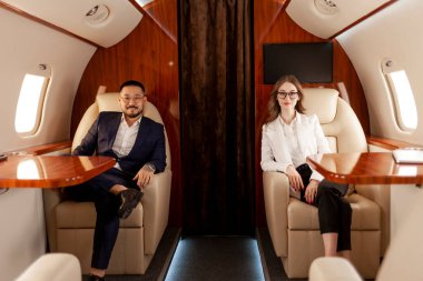 İş adamları özel lüks uçakla uçuyor, Asyalı iş adamı takım elbiseli ve kadın yönetici uçakta oturuyor ve buluşmaya uçuyorlar.