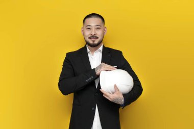 Takım elbiseli Asyalı inşaat mühendisi elinde sarı izole edilmiş arka plan planları olan evraklar, sıkı şapkalı ve iş elbiseli Koreli adam, mimar işçi