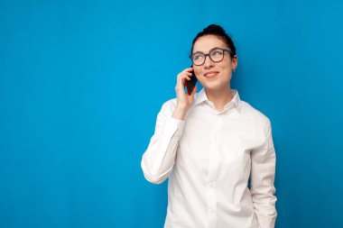 Beyaz gömlekli bir işletme yöneticisi mavi arka planda telefonla konuşuyor. Kız ofis çalışanı cep telefonuyla iletişim kuruyor.