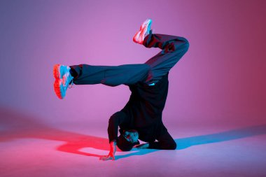 Genç erkek dansçı neon ışıkta dans ediyor, erkek akrobat kırmızı arka planda dans ediyor, hip hop sanatçısı hareket ediyor ve elleri üzerinde duruyor.