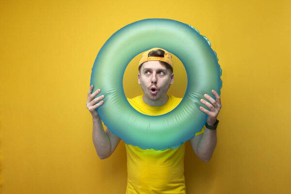 молодой удивленный парень турист в летней одежде и очках держит плавательное кольцо и смотрит в него и удивляется, отпуск концепции путешествия