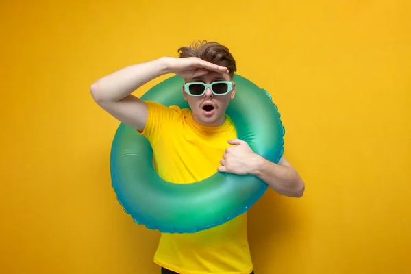 young guy in summer clothes with a swimming inflatable ring looks into the distance, the concept of traveling to the sea