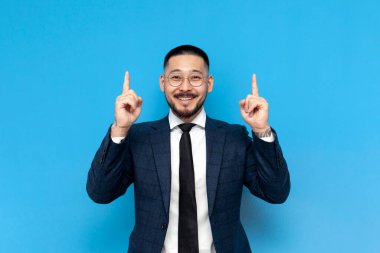 Mavi arka plandaki başarılı Asyalı işadamı ellerini kaldırdı ve boş alana işaret etti. Koreli girişimci iş kıyafetleri reklamları için yukarıdan alan kopyaladı.