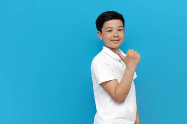 Beyaz tişörtlü küçük Asyalı çocuk mavi arkaplanı işaret ediyor, Koreli çocuk izole arka planda fotokopi alanı reklamları yapıyor.