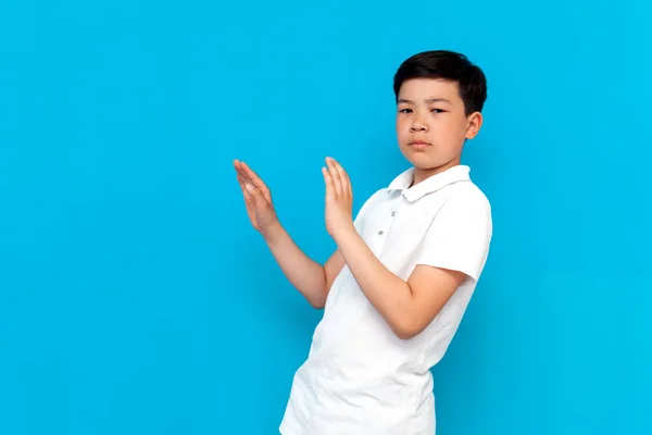 little asian boy in white t-shirt avoids and refuses on blue background, korean child shows disgust and withdraws on isolated background