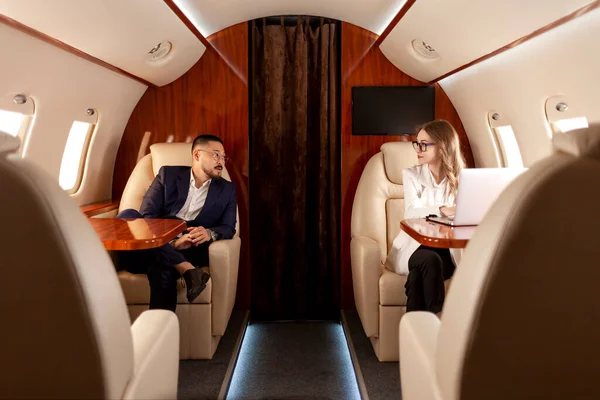 business people are flying in private luxury plane, asian businessman in suit and woman manager are sitting in plane and flying to meeting