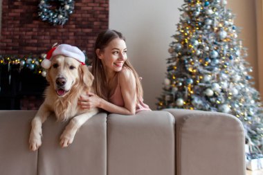 Yeni yıl ağacının yanında Noel Baba şapkalı ve fotokopi alanına bakan genç tatlı bir kız. Golden Retriever ile birlikte yeni yılı kutlayan bir kadın.