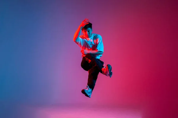 stock image male dancer jumps and flies in the air, young guy hiphop performer break dances in neon club lighting and does acrobatic stunt