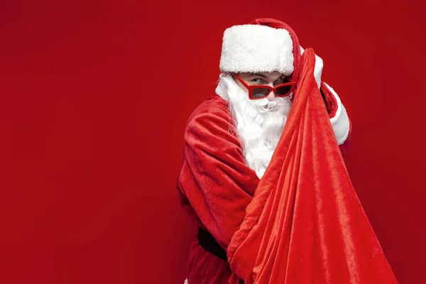 Święty Mikołaj Świątecznych Okularach Kapeluszu Wyciąga Prezenty Torby Czerwonym Tle — Zdjęcie stockowe